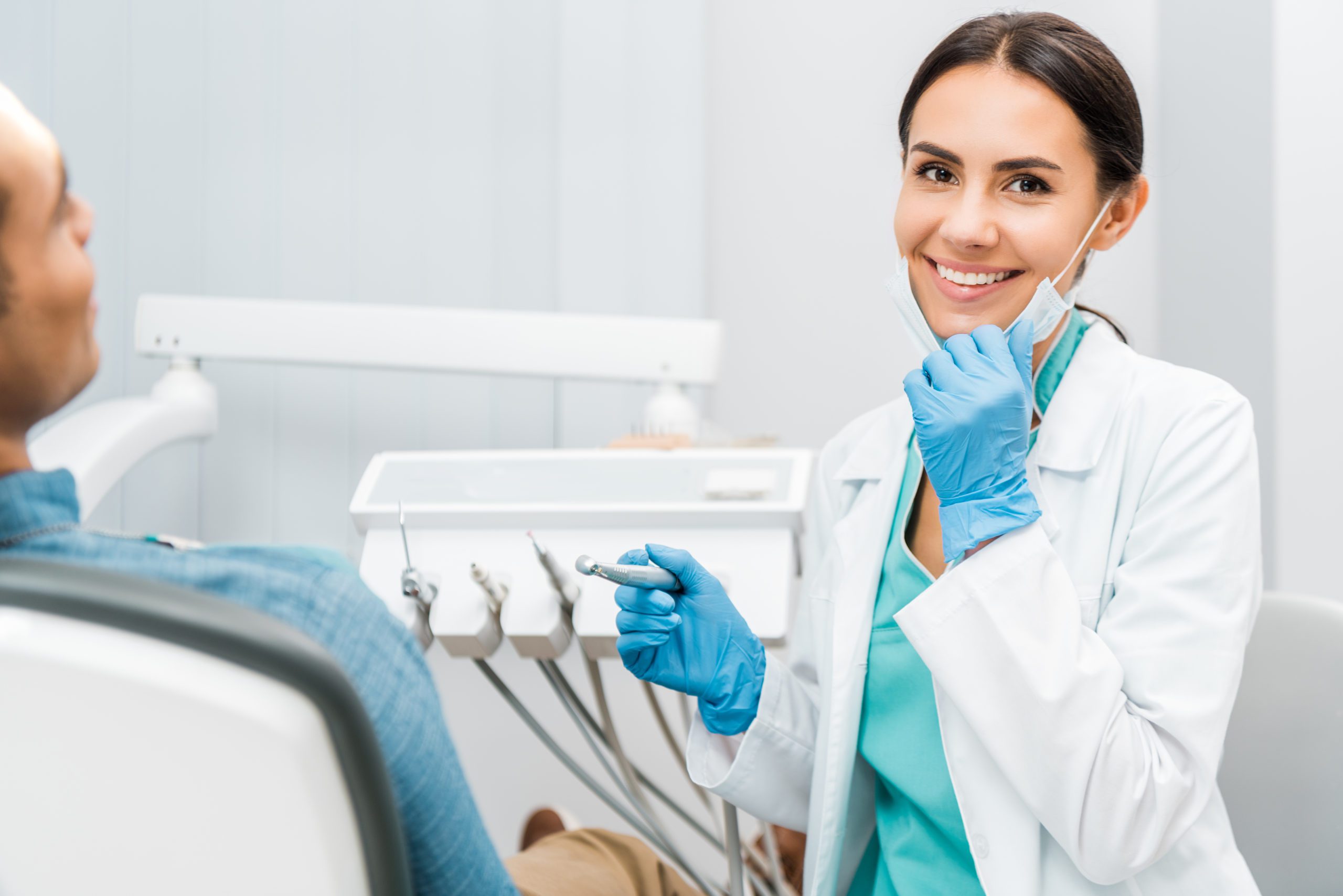Cheerful female dentist holding drill and smiling near patient